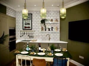 Imnage of a kitchen dining room with white masonry tiles, a dining table set for six, and three overhead lights.