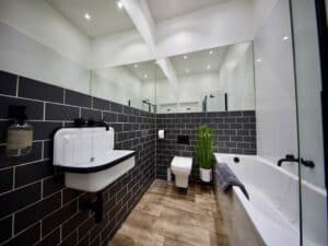 Swish bathroom with black tiles in a masonry formation, and a wooden floor and a plant in the corner.