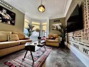 Living room decorated tastefully with beige sofas and sage green walls and a palm by the bay window