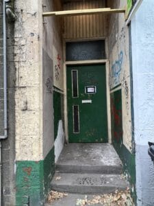 A uninviting front door of a flat with graffiti on the surrounding walls.