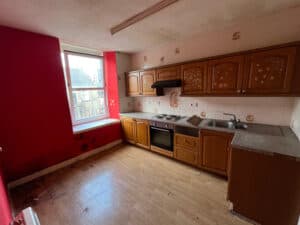 A dark, dingy kitchen with dated units and red walls